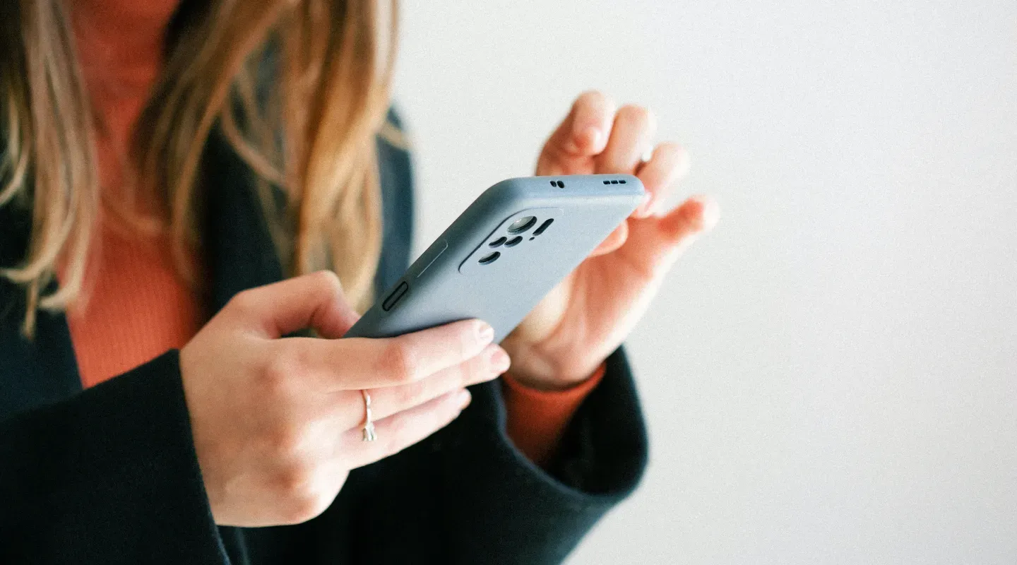 Mujer sosteniendo un teléfono con ambas manos.