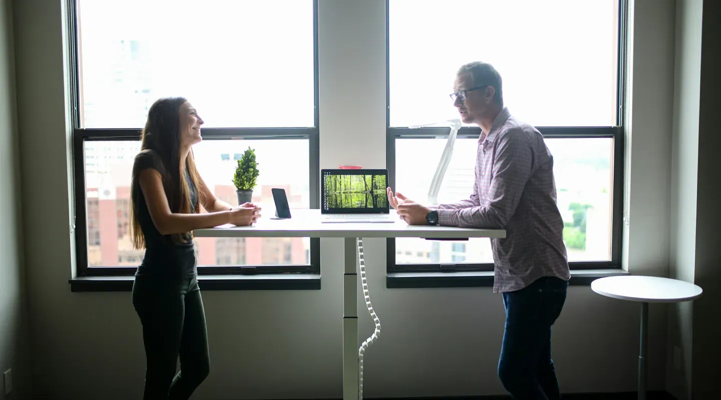 Dos personas conversando de pie y apoyados en una mesa.